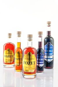 Steklenice medeni likerjev Sladek Greh na leseni mizi z medom in čebelami v ozadju